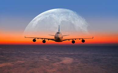 Airplane flying above tropical sea at sunset, full moon in the background 