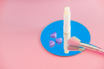 Wall Mural - Multi-colored makeup brush, white lipstick and little purple hearts on a round mirror with reflection in pink and blue colors