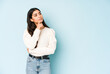 © Asier - Young indian woman isolated on blue background looking sideways with doubtful and skeptical expression.