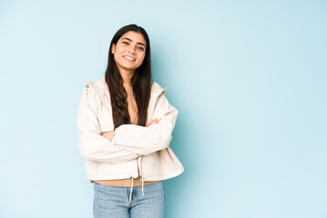 Wall Mural - Young indian woman on blue background who feels confident, crossing arms with determination.