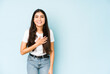 © Asier - Young indian woman on blue background laughs out loudly keeping hand on chest.