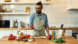 © Svitlana - Young man, Italian cook in apron holding, looking at tomato ready for preparing healthy meal with vegetables in the kitchen. Cooking at home concept