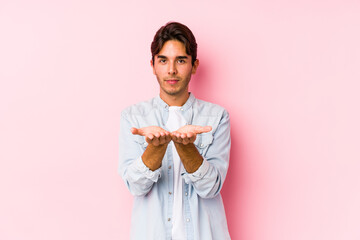 Wall Mural - Young caucasian man posing in a pink background isolated holding something with palms, offering to camera.