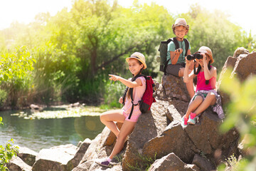 Wall Mural - school holidays. group of happy children sitting on rocks near river