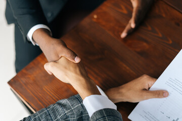 Close-up view of handshaking of black and white man hands after signing of successful business contract at the office. Concept of teamwork young business people.