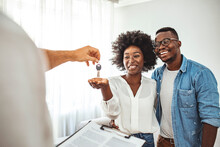 Couple Getting Keys From Realtor Of Their New Home. Portrait Of Financial Adviser Congratulating To A Young Couple For Buying A New House. African-American  Family Buy New House