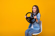 Profile photo of pretty funny lady good mood sit chair hold steering wheel ride imagine car drive license examination excited wear casual denim shirt isolated yellow color background