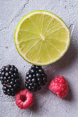 Wall Mural - Citrus lime slice, raspberry and blackberry berries, healthy summer fruits on stone concrete background, top view macro