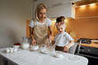 © Alexandr - happy mother baking with little daughter in apron and cook hat working with flour , bowl and spoon preparing dough teaching the kid baking and having fun together.