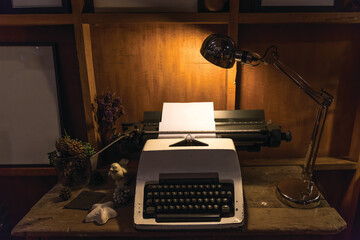 The old typewriter on the wooden desk under the light of the lamp background.