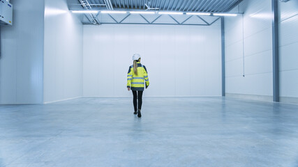 Poster - Female Engineer Wearing Safety Hat Walks Across Empty Factory Floor, Inspecting, Planning Future Factory Layout. Professional Industrial Designer Strategizing about New Manufacturing Plant Design