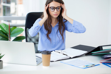 Wall Mural - Young office worker sitting at desk holding head because of pain in office