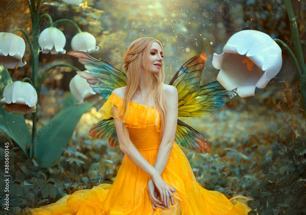 Portrait of happy fantasy woman blonde forest fairy. Fashion model in a bright yellow dress with butterfly wings sits posing in nature. Large flowers scenery decor white lilies. Light magic radiance. Stock Portrait of happy fantasy woman blonde forest fairy. Fashion model in a bright yellow dress with butterfly wings sits posing in nature. Large flowers scenery decor white lilies. Light magic radiance. Stock