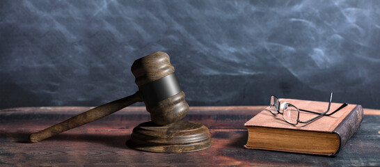 Wall Mural - Judge gavel, old books and reading glasses on a wooden table, black board background. 3d illustration