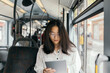 © Javier Pardina/Stocksy - Asian woman in a transport public, with tablet at morning.