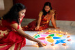 © SAPTAK GANGULY/Stocksy - Indian women lighting oil lamps during diwali and decorating with rangoli