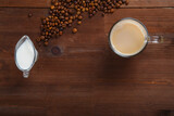 Fototapeta Mapy - A mug of coffee with milk and a jug of cream on the table among the scattered coffee beans.