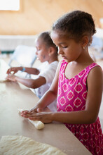 Sisters Rolling And Shaping Raw Pretzel Dough Into Different Shapes And Letters