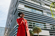 © MyMicrostock/Stocksy - Enthusiastic black woman in red coat discussing on smartphone in downtown