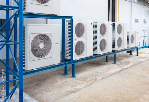 Condenser unit or compressor outside industrial plant building. Unit of central air conditioner (AC) or heating ventilation air conditioning system (HVAC). Electric fan and refrigerant pump inside.