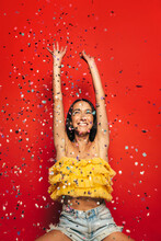 Cheerful Young Woman Throwing Confetti Over Red Background