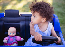 Pretty Toddler Girl With Curly Hair Sitting In Her Toy Car With Her Baby Doll