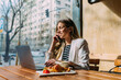 © MyMicrostock/Stocksy - Confident businesswoman using cellphone and laptop in cafeteria.
