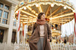 © Ivan Ozerov/Stocksy - portrait of a charming girl in a brown coat next to a carousel