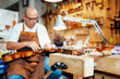 © Javier Ballester/ADDICTIVE STOCK - Selective focus of detail of wooden luthier workbench in workshop with blurred male artisan repairing violin