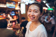 © Juan Alberto Ruiz/ADDICTIVE STOCK - Cheerful young Asian female in casual clothing looking at camera and smiling friendly while standing near illuminated street cafe in evening city