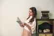 © Luis Gomez/ADDICTIVE STOCK - Side view of positive young female in stylish outfit leaning back on vintage cabinet and reading interesting book in cozy room