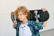 © Philippe Degroote/ADDICTIVE STOCK - Portrait of a blond boy with curly hair in summer clothes carrying a skateboard on his back and looking at the camera with a serious expression