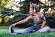 © Sergio Victor Vega/ADDICTIVE STOCK - Happy young ethnic female with curly hair in sportswear listening to music with headphones and smartphone and doing seated forward bend exercise while stretching body during fitness training in summer park