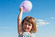© Sofia Roncero/ADDICTIVE STOCK - Smiling little child in summer dress standing with balloon in raised hand on background of blue sky and looking at camera