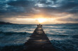 © Victor Prieto/ADDICTIVE STOCK - Silhouette of unrecognizable person standing on spectacular scenery of stormy sea with wooden quay under cloudy sky during sundown in Playa de Alcudia