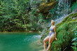 © Alberto Garrido/ADDICTIVE STOCK - Side view of serene female in bikini leaning on rock and enjoying view of amazing waterfall in forest