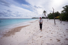 Full Body Front View Of Young Asian Female Traveler Walking On Tropical Beach With White Sand And Blue Sea Water While Spending Summer Holidays On Bodufolhudhoo Island In Maldives