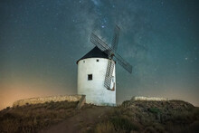 Low Angle Of Old White Windmill Tower Located On Hill Against Starry Night Sky With Milky Way