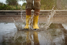 Detail Of Yellow Rain Boots Hitting A Puddle Splashing Water In A Path In The Forest