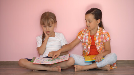 Wall Mural - Little girls reading a book in living room. Smart schoolgirls doing their homework after school. Education and distance learning for kids. Homeschooling during quarantine. Stay at home entertainment.