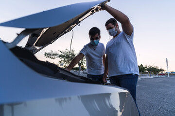 Dos hombres con mascarilla revisando motor de un coche