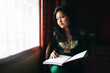 © saptak Ganguly/Stocksy - Beautiful teenage girl looking out the window with a open notebook in hand