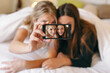 © BONNINSTUDIO/Stocksy - Two young roommates making a selfie with phone on the bedroom.