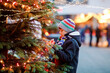© Irina Schmidt - Little cute kid boy having fun on traditional Christmas market during strong snowfall. Happy child enjoying traditional family market in Germany. Schoolboy standing by illuminated xmas tree.