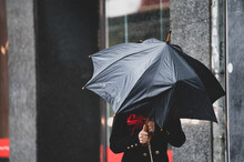 A Woman Has Difficulty Holding An Umbrella From Strong Winds In Rainy Weather.