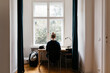 © Melanie Riccardi Photography/Stocksy - Woman sitting at Desk in front of window
