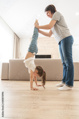 Fotografía Mother helping daughter to walk upside down on her arms at home holding legs