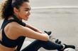 © Artem Varnitsin - Side view of a smiling woman sitting outdoors and resting after training