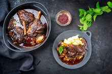 Modern Style Traditional Braised Slow Cooked Lamb Shank In Red Wine Sauce With Shallots And Mashed Potatoes Offered As Top View On A Design Cast Iron Plate And Pot