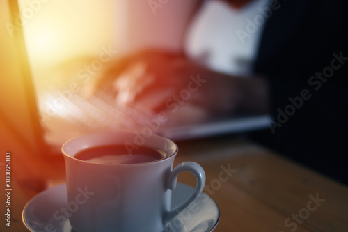 Person typing on laptop in dark condition, writer work on computer, focus on coffee with blur defocused background